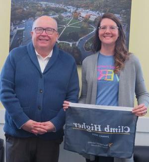 Jennifer Dietz stands to the left of Chris Gilmer, holding the "Climb Higher" banner